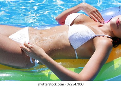 Sexy girl in white bathing suit. Wet body of young girl on mattress in the pool. Drops of water on tanned skin