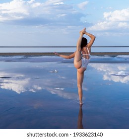 sexy girl in white on the mirror surface of the salt lake. flexible gymnast performs split among the clouds