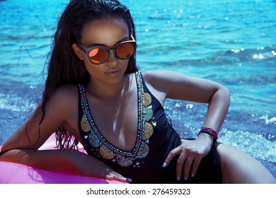 Sexy Glamour Model With Long Wet Hair In Black Swimsuit And Sunglasses Lying On Inflatable Circle . Shot On The Beach, Horizontal