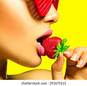 Sexy Glamour Woman wearing Fashion Sunglasses, Eating Strawberry. Sensual Lips. Manicure and Lipstick. Desire. Sexy red Lips with Strawberry over bright yellow background