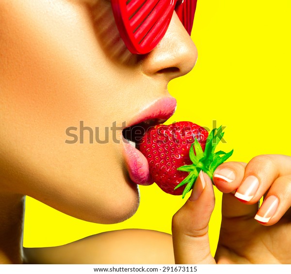 ファッションサングラスをかけ イチゴを食べるセクシーな女性 官能的な唇 マニキュアと口紅 欲望 明るい黄色い背景にセクシーな赤い唇とイチゴ の写真素材 今すぐ編集