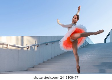 Sexy Graceful Slim Professional Caucasian Ballet Dancer in Rose Pink Tutu Dreass Whie Posing In Dance Flying Pose On Blue Stairs In Stretched Pose Outdoor. Horizontal Image Orientation