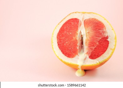 Sexy grapefruit with sperm, erotic concept. Sectional grapefruit is a symbol of the vagina and clitoris. Half grapefruit with dripping white liquid on a pastel background. Erotic concept.