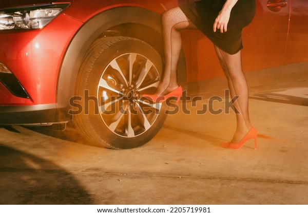 sexy\
legs in black fishnet stockings and red high heels, leaning on the\
wheel of a red car, at sunset time,\
horizontal\
