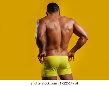 Sexy Male Back. The Back View Of Torso Of Attractive Male Body Builder On Yellow Background. Rear View Of A Bare-chested Muscular Young Man In Sexy Panties Underwear