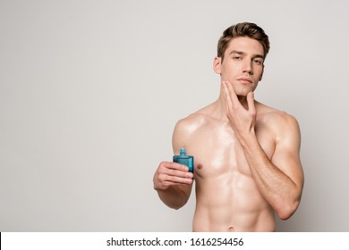sexy man with muscular torso applying aftershave on face isolated on grey
