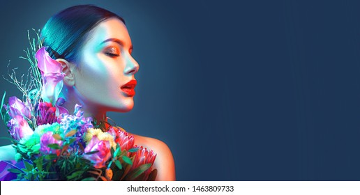 Sexy model girl with fashion bouquet of beautiful flowers in colourful fashion lights. Party. Beauty young woman with design bunch of flowers celebrating in Colorful neon lights, floral art design.