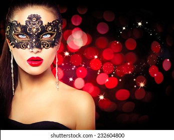Sexy model woman in venetian masquerade carnival mask at party over holiday glowing red background. Christmas and New Year celebration. Glamour lady