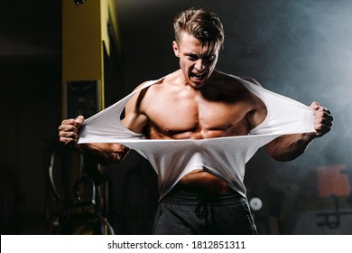 Sexy muscular man ripping shirt in gym emotionally and furious. Hot and handsome man tearing shirt with anger and furious. Fitness motivation background