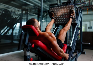 Sexy muscular men using a leg press machine and placing his legs on the platform on a dark colorful background.