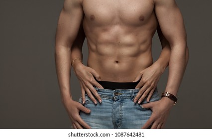 Sexy Muscular Naked Man And Female Hands Unbuckle His Jeans On A Dark Background