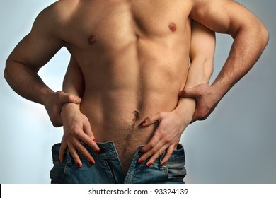 Sexy muscular naked man and female hands unbuckle his jeans