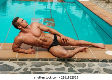 Sexy muscular young man in black speedo lying near swimming pool