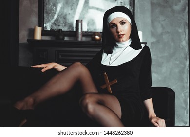 Sexy nun prays indoor . Beautiful young holy sister. Young beautiful nun with a cross in a robe in a black interior.