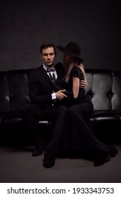 Sexy Passionate Couple In Elegant Evening Dresses On A Dark Sofa In A Room With Low Light