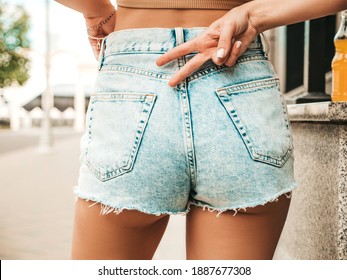 Sexy perfect female buttocks on the street city background. Woman in jeans shorts holding her hands in pockets. Model shows peace sign. No face, unrecognizable