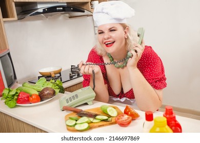 Sexy Pinup Plus Size Caucasian Woman In Cook's Hat Talking By Phone And Making Salad And Healthy Food On The Kitchen, Stay At Home. Concept Of Body Positivity