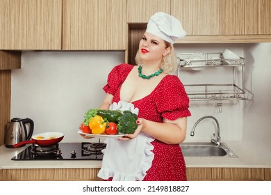 Sexy Pinup Plus Size Caucasian Woman In Cook's Hat With Vegetables On The Kitchen, Stay At Home Concept. Healthy Food For Oversized