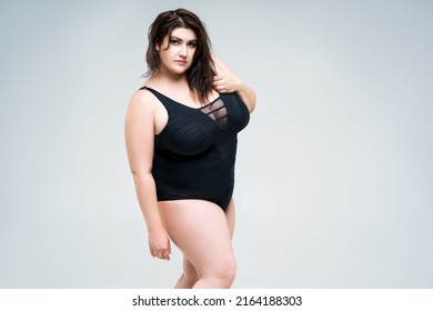 Sexy plus size fashion model in black one-piece swimsuit, fat woman in lingerie on gray background, body positive concept