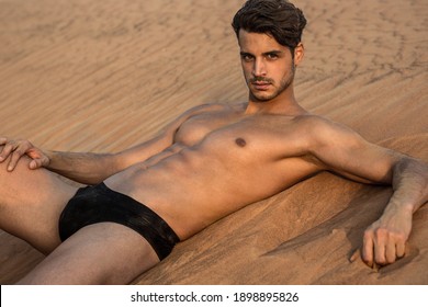 Sexy portrait of male model lying naked in the desert sand wearing underwear.
