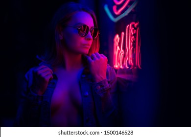 Sexy portrait of a young girl with an open bust in sunglasses and with in the night city, red-blue light of neon lamps. Night clubs, parties, strip business, night life, business game. Banner