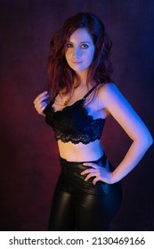 sexy red-haired girl in black bra and black leather trousers in a photo studio with a dark red background