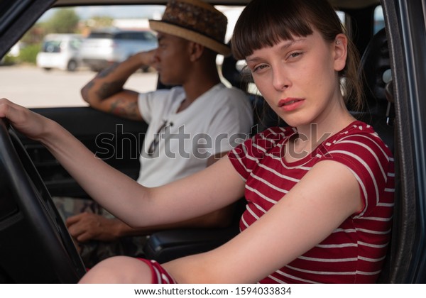 Sexy serious\
Beautiful young Girl sitting on Front Seat of a Car with friend\
driving and looking in\
camera