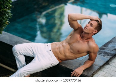 Sexy Shirtless Man In  White Pants With Athletic Body Posing On Swimming Pool. Muscular Sports Male Model. 