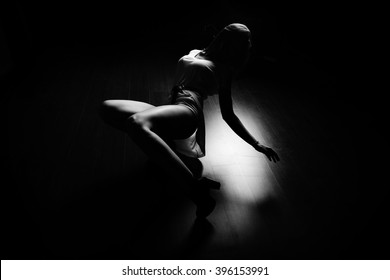 Sexy slim woman dancing in the dark on floor, wearing long white shirt and high heels