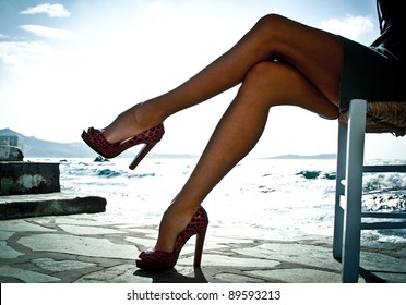 Sexy summer legs in high heels by the sea in Mykonos, Greece. Backlit image.