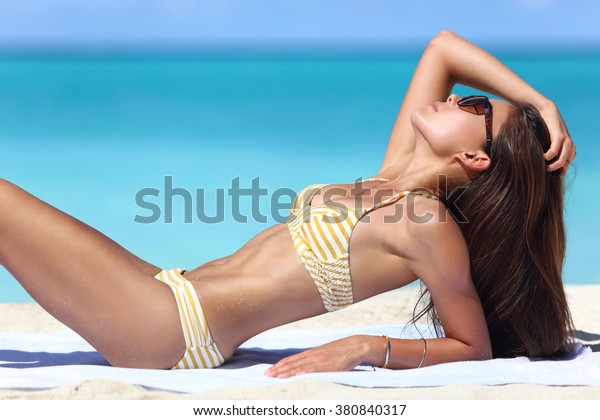 ファッションビキニで日に当たるセクシーなサンタンビーチ女性 タオルでなめしをくつろぐ美しい体型 痩せるか 肌の手入れをする日焼け防止のコンセプト の写真素材 今すぐ編集