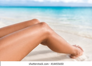 Sexy suntan bikini woman legs relaxing lying down on white sand beach summer vacation. Beauty skincare sun aging protection body care of tanned skin. Epilation laser or shaving concept.
