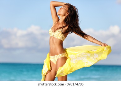 Sexy suntan woman relaxing enjoying sunset on beach with beachwear cover-up wrap showing slim bikini body for weight loss and skin care epilation concept. Asian model sunbathing during summer holiday.