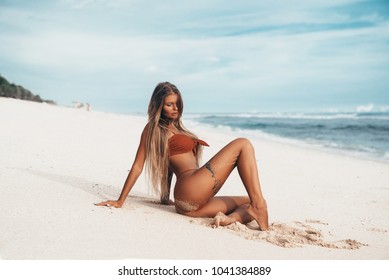 Sexy tattooed young girl in red swimsuit posing on the beach. Beautiful blonde woman with long hair relaxing at the ocean. Concept of sporty model, swimwear