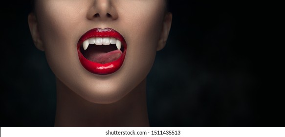 Sexy Vampire Woman's red bloody lips close-up. Vampire girl licking fangs with tongue. Fashion Glamour Halloween art design. Close up of female vampire mouth, teeth. Isolated on black background