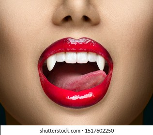 Sexy Vampire Woman's red bloody lips close-up. Vampire girl licking fangs with tongue. Fashion Glamour Halloween art design. Close up of female vampire mouth, teeth. Vampire woman teeth closeup