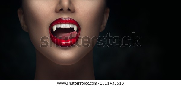 Sexy Vampire Woman\'s red bloody lips close-up.\
Vampire girl licking fangs with tongue. Fashion Glamour Halloween\
art design. Close up of female vampire mouth, teeth. Isolated on\
black background