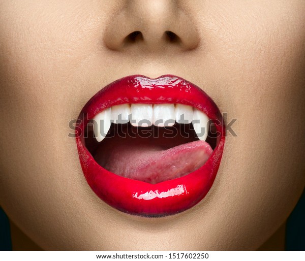 セクシーな吸血鬼女の赤い血色の唇の接写 舌で牙を舐める吸血鬼の女の子 ファッショングラマーハロウィーンのデザイン 女性の吸血鬼の口の接写 歯 吸血鬼の女の歯の接写 の写真素材 今すぐ編集