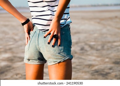 Sexy woman body in jean shorts. The model is back.Tan lady with perfect body posing outdoor. Wearing jeans stylish shorts and striped shirt .