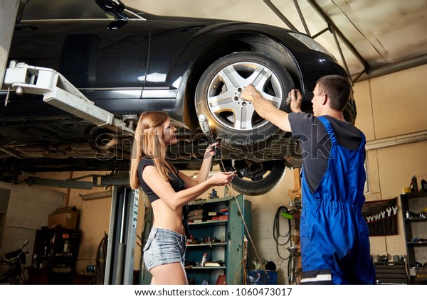 Sexy\
woman helps an auto mechanic repair a car on hydraulic lift . Girl\
in a frank dressed have a perfect body. Car\
Workshop