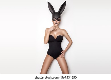 Sexy woman with large breasts wearing a black mask Easter bunny standing on a white background and looks very sensually