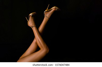 Sexy woman legs. Woman legs in gold shoes in black background. Long legs woman with high heels shoes