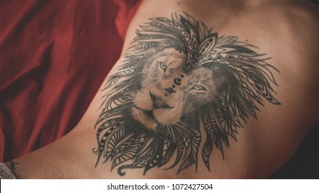 Sexy woman with lion tattoo at her back lying on red linen