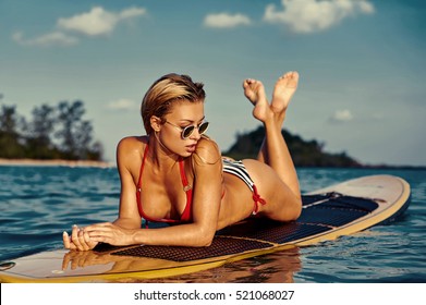 Sexy woman lying on a surfing board on the water in the sea