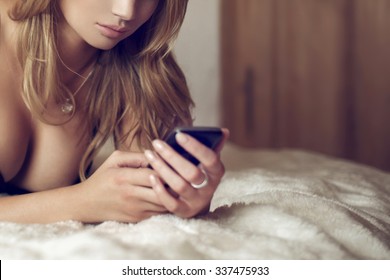 Sexy woman on bed write message by phone, closeup