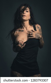 Sexy woman studio portrait with black dress and tattoos against dark background.