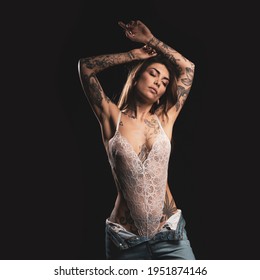 Sexy woman studio portrait with white lingerie and tattoos against dark background.