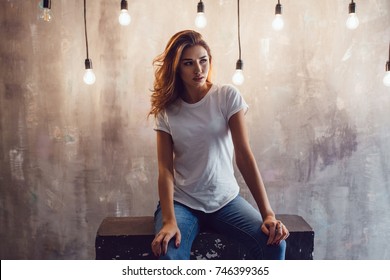 Sexy woman in a white T-shirt on a gray background with light bulbs. Mock-up.