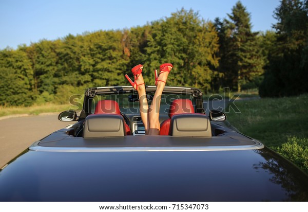Sexy woman\'s\
legs with red shoes showing out of the car, enjoying freedom.\
Attractive legs in the cabrio. Woman relaxing in a car. Summer\
vacations concept. Space for\
text.