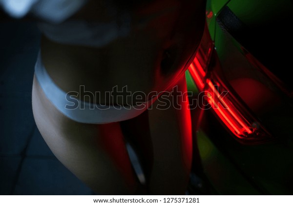 Sexy women stay near\
supercar rear taillight. Woman\'s body is illuminated by a car red\
light